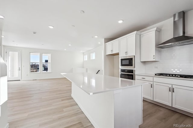 kitchen featuring a center island, stainless steel oven, white cabinets, wall chimney exhaust hood, and built in microwave