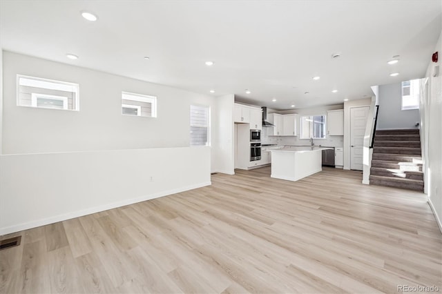 kitchen with dishwasher, a center island, wall chimney range hood, light hardwood / wood-style floors, and white cabinetry