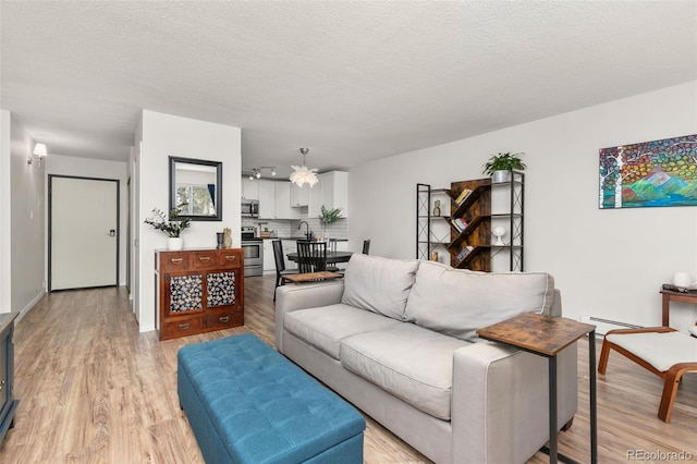 living room with a textured ceiling, light wood finished floors, baseboard heating, and baseboards