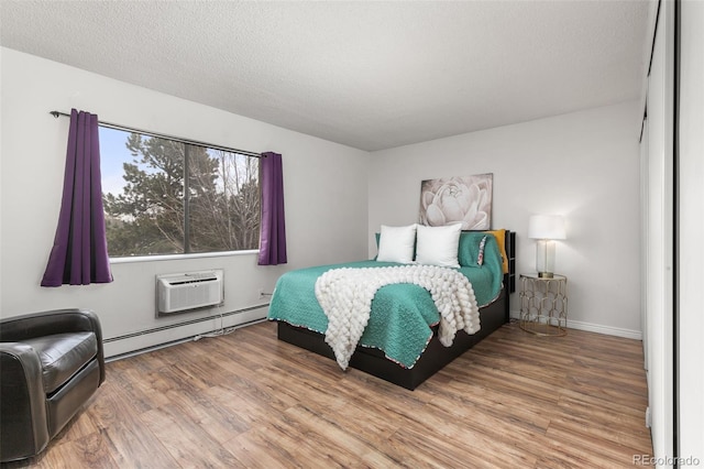 bedroom featuring a textured ceiling, a wall mounted AC, a baseboard heating unit, and wood finished floors