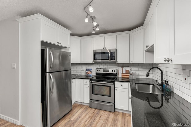 kitchen featuring white cabinets, appliances with stainless steel finishes, a sink, a textured ceiling, and light wood-type flooring