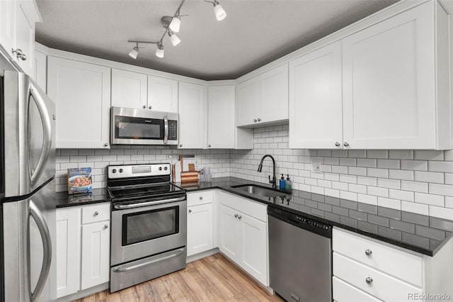kitchen with a sink, tasteful backsplash, light wood-style flooring, white cabinets, and appliances with stainless steel finishes