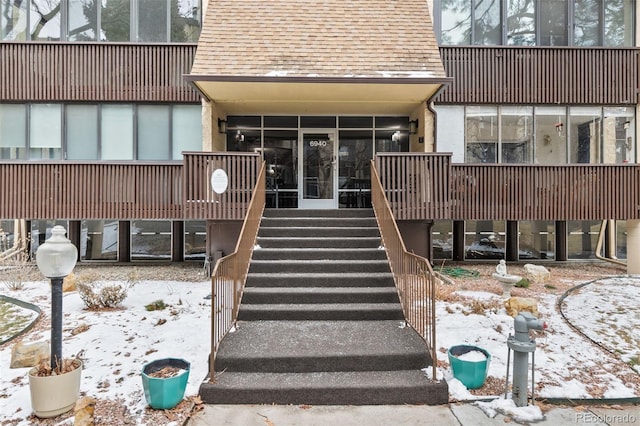 snow covered property entrance featuring roof with shingles