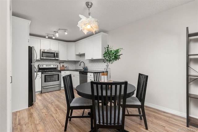 kitchen with white cabinets, tasteful backsplash, a sink, light wood finished floors, and appliances with stainless steel finishes