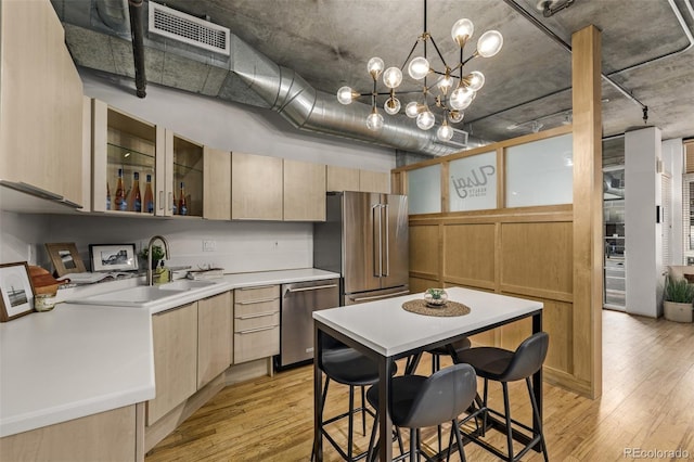 kitchen with appliances with stainless steel finishes, light brown cabinets, light hardwood / wood-style floors, and hanging light fixtures