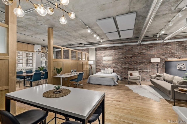 dining room featuring a chandelier, rail lighting, light hardwood / wood-style flooring, and brick wall