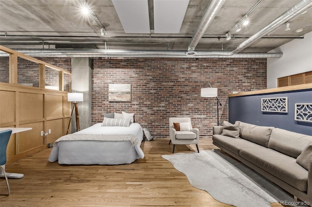 bedroom with hardwood / wood-style floors, brick wall, and track lighting