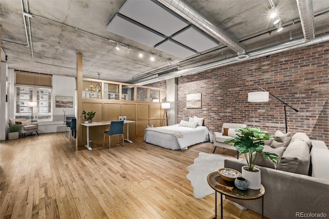 bedroom with rail lighting, brick wall, and light wood-type flooring