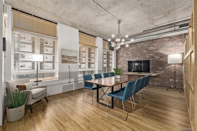 dining space with an inviting chandelier, brick wall, and light hardwood / wood-style flooring