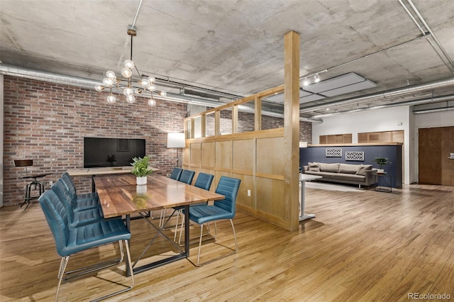 dining space featuring brick wall, light hardwood / wood-style floors, and a notable chandelier