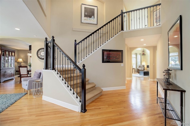 interior space with a towering ceiling, light wood-style flooring, arched walkways, and baseboards