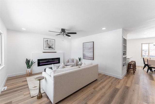 living room featuring built in shelves, light hardwood / wood-style flooring, and ceiling fan