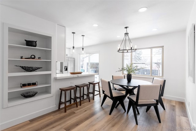 dining space with built in features, light hardwood / wood-style floors, and a notable chandelier