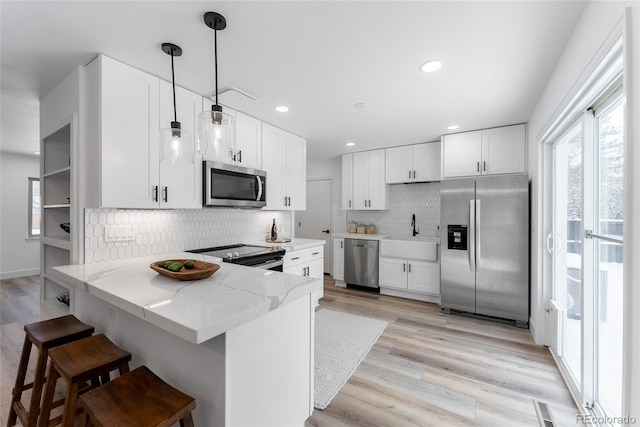 kitchen featuring white cabinets, sink, hanging light fixtures, light stone counters, and stainless steel appliances