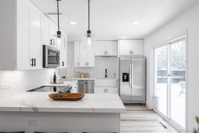 kitchen with hanging light fixtures, stainless steel appliances, light stone counters, kitchen peninsula, and white cabinets