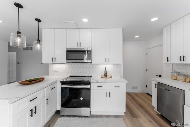 kitchen with tasteful backsplash, appliances with stainless steel finishes, pendant lighting, white cabinets, and light wood-type flooring