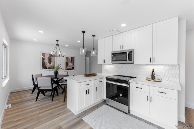 kitchen featuring kitchen peninsula, appliances with stainless steel finishes, decorative light fixtures, and white cabinets