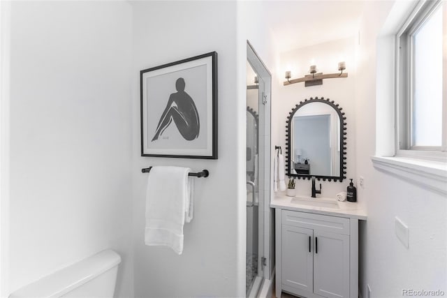 bathroom featuring a shower with door, vanity, and toilet