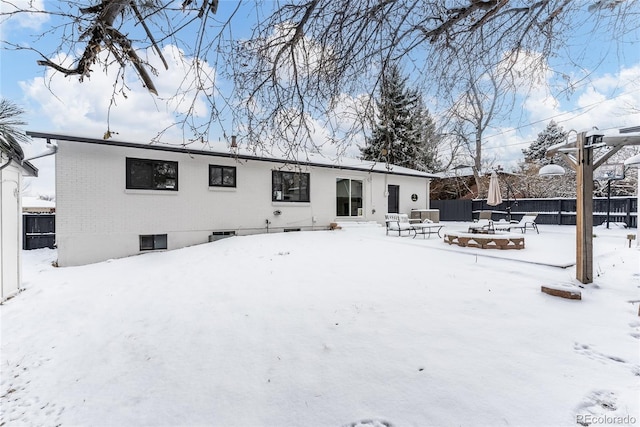 snow covered house featuring an outdoor fire pit, fence, and brick siding