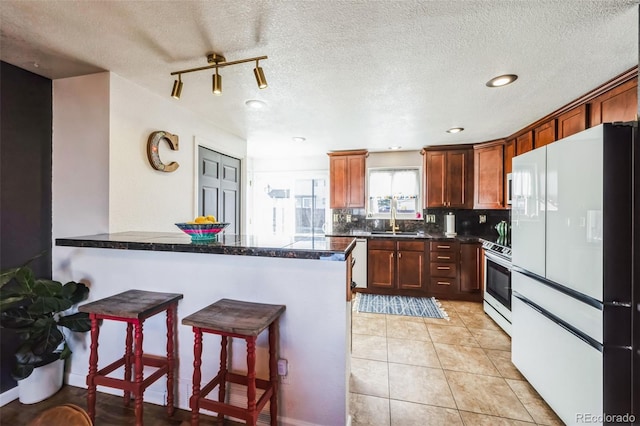 kitchen featuring white refrigerator, sink, stainless steel range with electric cooktop, tasteful backsplash, and kitchen peninsula