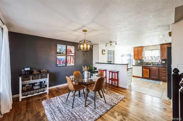 dining room featuring sink, a textured ceiling, light wood-type flooring, and a notable chandelier