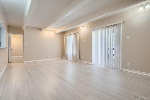 spare room with a textured ceiling, baseboards, light wood-style floors, beamed ceiling, and plenty of natural light