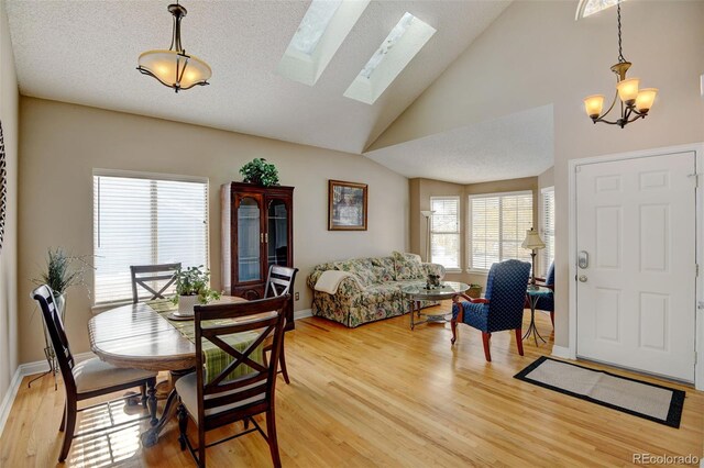 dining area featuring vaulted ceiling with skylight, a chandelier, a textured ceiling, and light hardwood / wood-style flooring