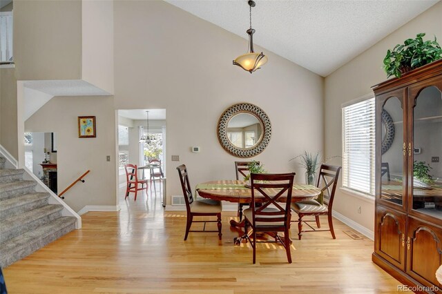 dining area featuring light wood-type flooring, a chandelier, and high vaulted ceiling