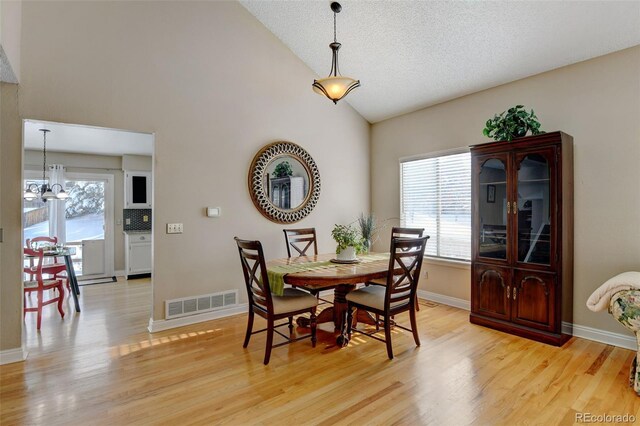 dining space with light hardwood / wood-style floors, a chandelier, a textured ceiling, and high vaulted ceiling