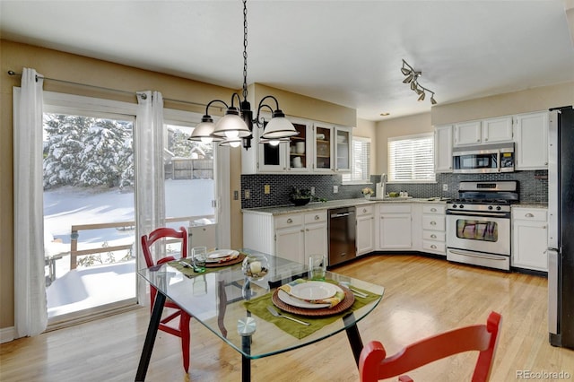 kitchen with light wood-type flooring, appliances with stainless steel finishes, hanging light fixtures, decorative backsplash, and white cabinets