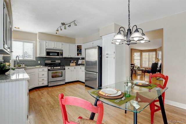 kitchen with stainless steel appliances, hanging light fixtures, plenty of natural light, and white cabinets