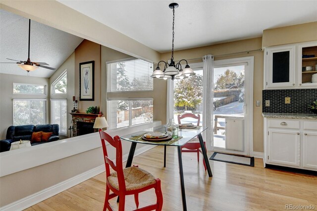 dining area featuring ceiling fan with notable chandelier, light wood-type flooring, and vaulted ceiling