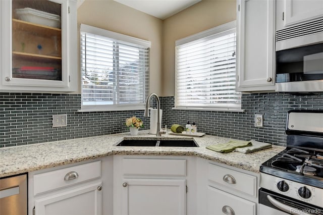 kitchen with sink, appliances with stainless steel finishes, light stone countertops, white cabinets, and decorative backsplash