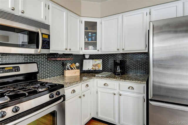 kitchen featuring white cabinetry, decorative backsplash, stainless steel appliances, and light stone countertops