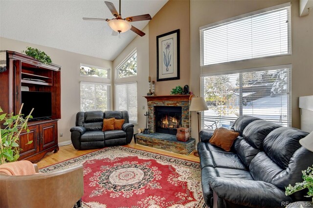 living room with ceiling fan, wood-type flooring, a stone fireplace, and high vaulted ceiling