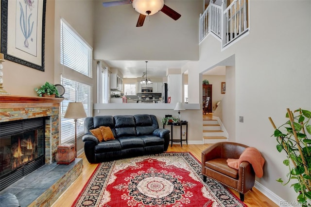 living room featuring a high ceiling, ceiling fan, a stone fireplace, and light hardwood / wood-style floors