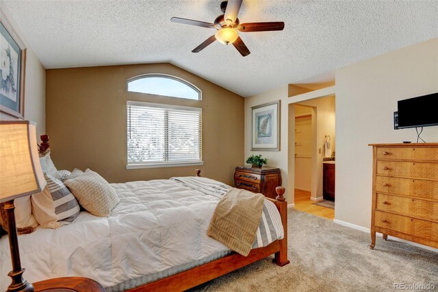 carpeted bedroom featuring ceiling fan, ensuite bath, a textured ceiling, and lofted ceiling