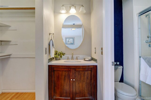 bathroom with hardwood / wood-style flooring, a shower with door, vanity, and toilet