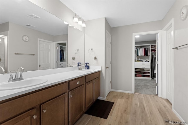 full bath featuring a sink, double vanity, wood finished floors, and a spacious closet