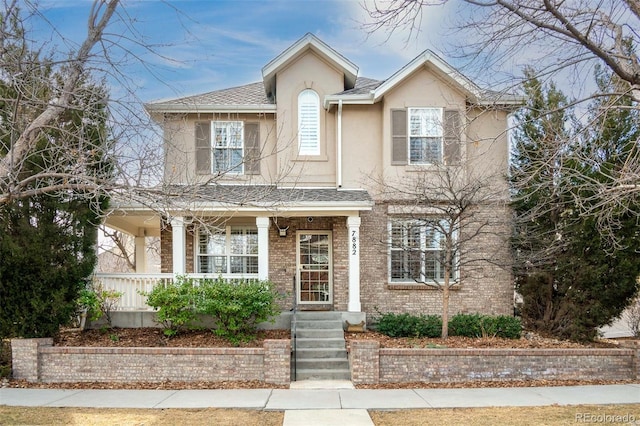 view of front of home with covered porch, roof with shingles, brick siding, and stucco siding