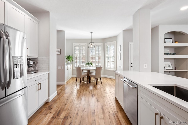 kitchen featuring white cabinets, light countertops, appliances with stainless steel finishes, light wood-type flooring, and decorative backsplash