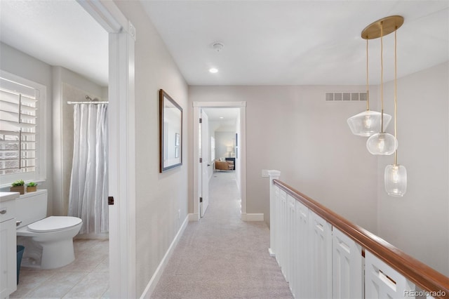 hall featuring light tile patterned flooring, light carpet, an upstairs landing, visible vents, and baseboards