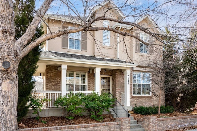 view of front of home with brick siding, roof with shingles, a porch, and stucco siding