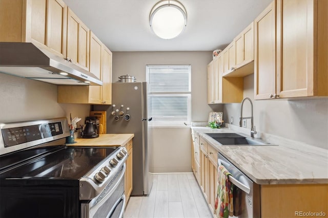 kitchen with light stone countertops, stainless steel appliances, under cabinet range hood, light brown cabinets, and a sink