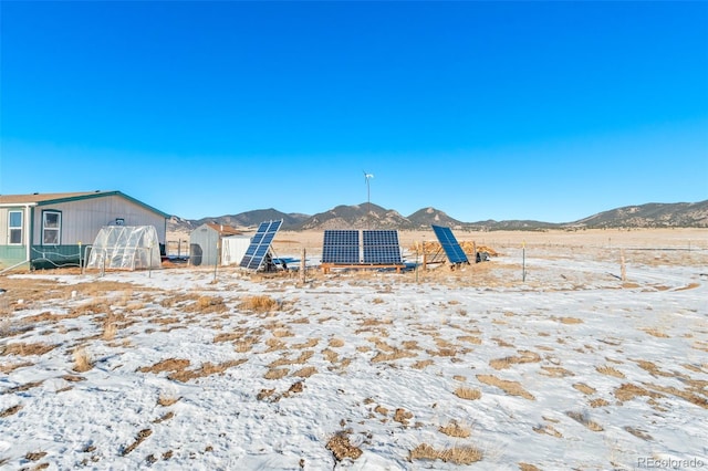 snow covered property with a mountain view and solar panels