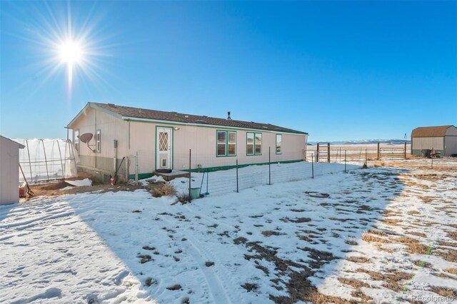 snow covered back of property featuring fence and a shed