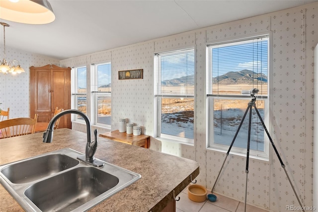 kitchen with a notable chandelier, light tile patterned floors, hanging light fixtures, a sink, and wallpapered walls