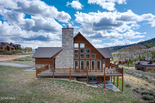 62 897, Grand Lake, CO 80447 - rear view of house featuring a deck with mountain view, a chimney, stone siding, and a lawn