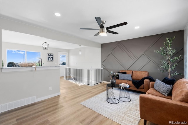 living room with ceiling fan with notable chandelier and light hardwood / wood-style flooring