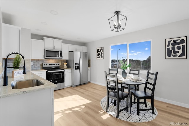 kitchen featuring sink, light hardwood / wood-style floors, pendant lighting, white cabinets, and appliances with stainless steel finishes